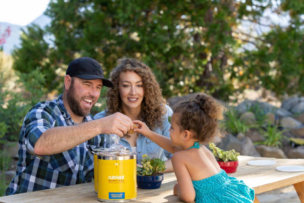A family sits at a table with a yellow juicer, ready to prepare their emergency food storage.