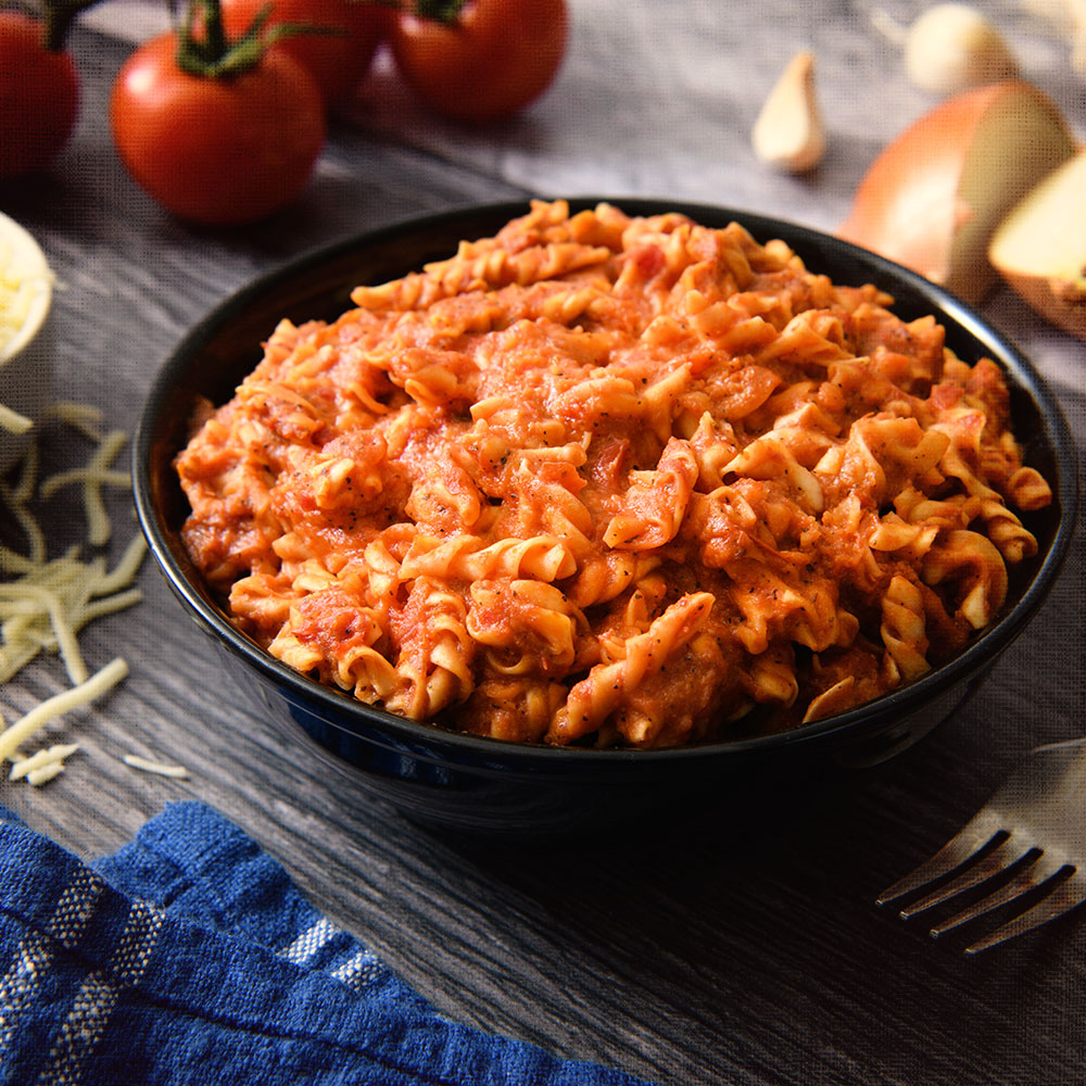 A bowl of Nutrient Survival Lasagna #10 Can - 10 Servings - (SHIPS IN 2-4 WEEKS) with sauce and tomatoes on a wooden table.