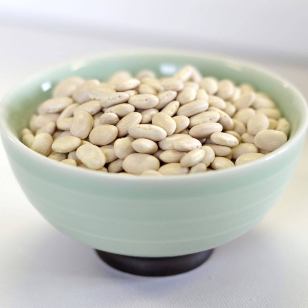 White beans in a bowl on a white surface.