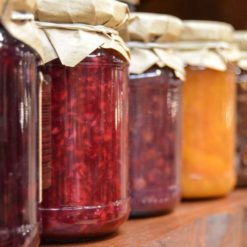 Jars of jam, ideal for emergency food storage, are lined up on a shelf.